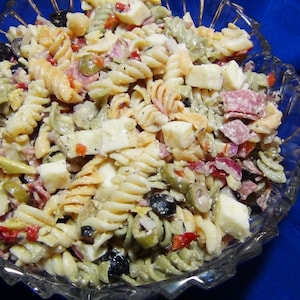 以下が含まれることがあります： モッツァレラチーズ、サラミ、オリーブ、赤ピーマンなど、さまざまな食材が入ったパスタサラダのボウルです。