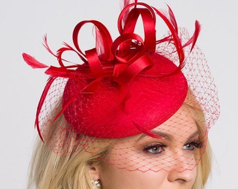 Può includere: Un cappello di feltro rosso con un nastro rosso e piume, e un velo di rete rosso.