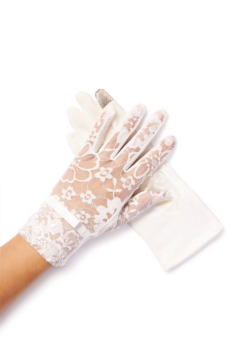 May include: A pair of white lace gloves with a floral pattern. The gloves are shown on a hand with the wrist portion of the glove folded back.