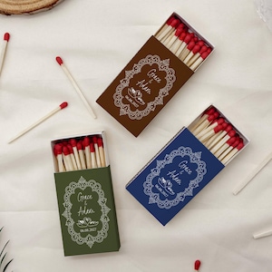 May include: Three rectangular matchboxes in brown, olive green, and navy blue, each containing wooden matches with red tips. The boxes feature a white ornate frame design with the text Grace & Adam and the date 08.08.2027 printed on the front.