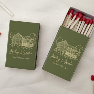 May include: Two olive green matchboxes featuring a gold line drawing of a house, the text Hailey & Jordan, and the date AUGUST 20th, 2027. One box is closed, and the other is open, revealing wooden matches with red tips inside the box.
