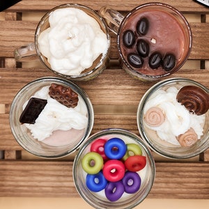 May include: Six glass jars with lids containing different scented wax melts. The wax melts are arranged in a wooden crate. The wax melts are shaped like coffee cups, doughnuts, and other treats. The jars are labelled "Star Beans Cafe".