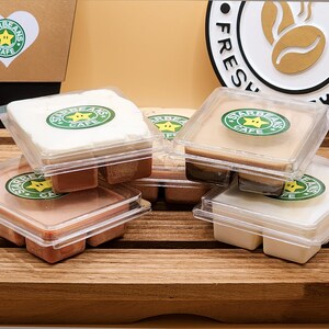 May include: Six wax melts in clear plastic containers with a brown, white and beige wax. Each container has a green and yellow logo that says "Starbeans Cafe" with a star and coffee bean.