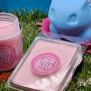 May include: A pink wax melt in a clear plastic container with a pink and white sticker featuring a cartoon pink cat. The sticker says "Vigilant Candles".