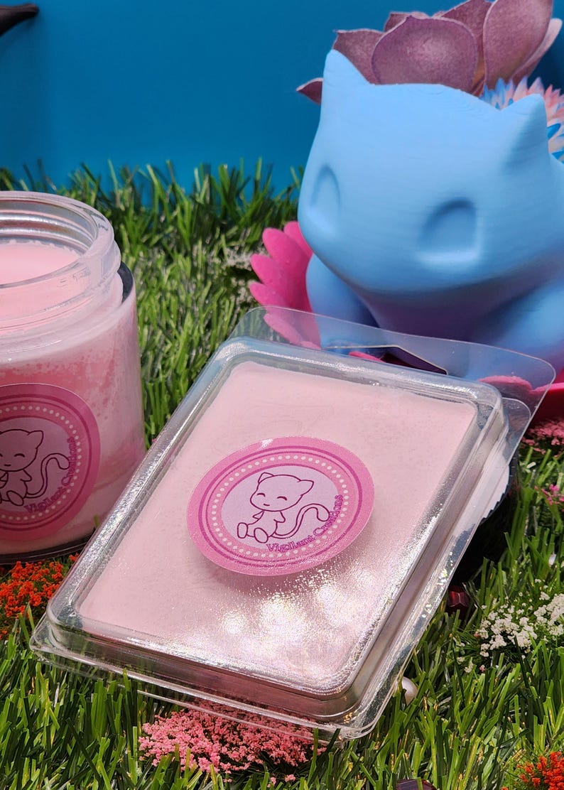 May include: A pink wax melt in a clear plastic container with a pink and white sticker featuring a cartoon pink cat. The sticker says "Vigilant Candles".