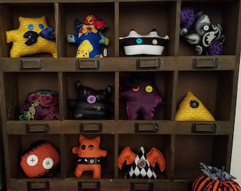 May include: A wooden shelf with 10 compartments, each containing a unique handmade plush toy. The toys are made from various fabrics and feature different colors, patterns, and designs.