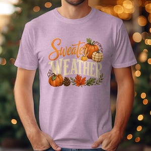 Light pink t-shirt with "Sweater Weather" graphic featuring pumpkins and autumn leaves.