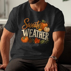 Dark crew neck t-shirt with "Sweater Weather" text and pumpkins, leaves, and pinecone graphic.