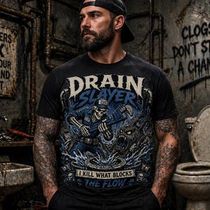 May include: Black t-shirt with a graphic featuring a skeleton plumber wielding tools, the words "DRAIN SLAYER" and "I KILL WHAT BLOCKS THE FLOW." The background includes graffiti and plumbing fixtures.