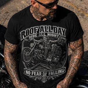 May include: Black t-shirt with a motorcycle graphic and the text "ROOF ALL DAY RIDE ALL NIGHT NO FEAR OF FALLING". The graphic features a skeleton riding a motorcycle. The person in the image is wearing sunglasses and has tattoos.