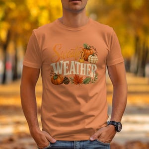 Orange t-shirt with "Sweater Weather" text and pumpkin, pinecone, and leaf graphic.