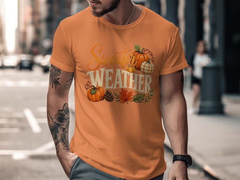 Orange t-shirt with "Sweeter Weather" text and pumpkins, pinecones, and fall leaves graphic.