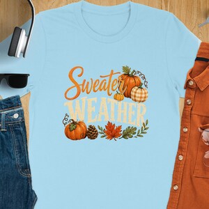 Light blue t-shirt with "Sweater Weather" text, pumpkins, leaves, and pinecone graphic.