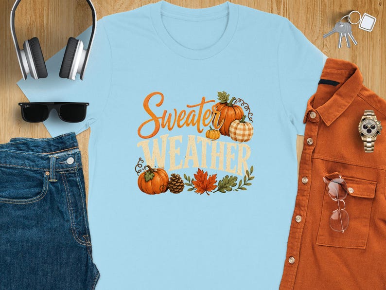 Light blue t-shirt with "Sweater Weather" text, pumpkins, leaves, and pinecone graphic.