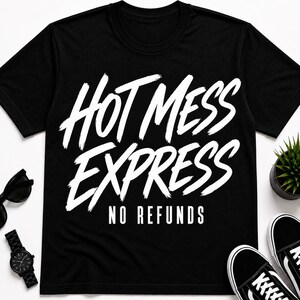 Könnte beinhalten: Ein schwarzes Kurzarm-T-Shirt mit dem weißen Schriftzug "HOT MESS EXPRESS" in einer fetten Pinselstrich-Schriftart, wobei die Worte "NO REFUNDS" in einer kleineren, klaren serifenlosen Schrift direkt unter der Grafik gedruckt sind.
