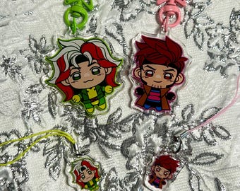May include: Two large acrylic keychains and two smaller phone charms featuring cartoon characters. One character has white and red hair in a green suit, the other has red hair and a brown coat. They include green and pink star-shaped clasps.
