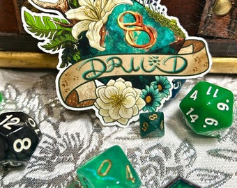 May include: A sticker with a floral and antler design and the word "DRUID" on a banner. Several green and black dice are scattered around the sticker, suggesting a tabletop gaming theme.