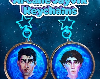May include: Two keychains featuring portraits of male characters with blue skin and dark hair, set against a blue cosmic background. The keychains have a gold-colored border and are attached to a star-shaped clasp. The text "Arcane Jayvik Keychains" is displayed at the top.