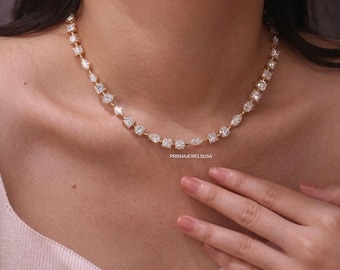 May include: A gold-toned necklace featuring a series of alternating clear, faceted stones in various shapes including round, square, pear, and marquise cuts. The jewelry piece is set on a thin metal chain and includes the text PRISHAJEWELSUSA.
