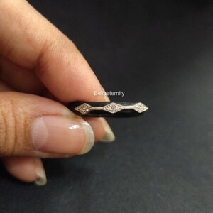 May include: A black ring with three diamond-shaped sections, each with small, sparkling stones. The ring is held against a dark background, showcasing the contrast of the shiny stones against the black band. The ring is a piece of jewelry.