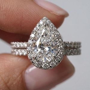 Peut inclure: Une bague de fiançailles en diamant en forme de poire, entourée d'un halo de petits diamants. La bague est sertie sur un anneau orné de petits diamants. La bague est un bijou.