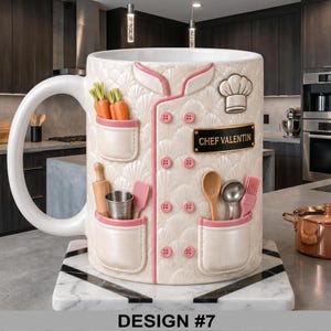 May include: A large white ceramic mug designed as a chef's jacket, featuring pink trim and buttons. The mug has pockets with miniature carrots, a rolling pin, and other kitchen tools. The text "CHEF VALENTIN" is on a black nameplate.