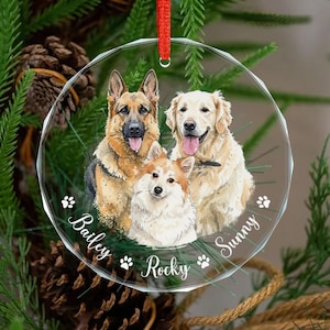 May include: A clear, round Christmas ornament with a red ribbon, featuring portraits of three dogs: a German Shepherd, a Golden Retriever, and a Corgi. The names "Bailey", "Rocky", and "Sunny" are written on the ornament.