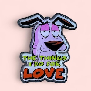 May include: A pin featuring Courage the Cowardly Dog with the phrase "THE THINGS I DO FOR LOVE." The pin has a pink background, a purple dog, and black and white accents. The text is in green and orange.