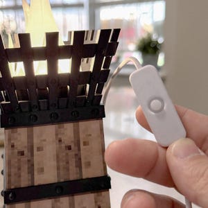 May include: A decorative lamp shaped like a torch, featuring a wooden base with metal accents and a glowing flame-shaped light. The lamp has a white cord with an on/off switch. The lamp is lit, casting a warm glow.