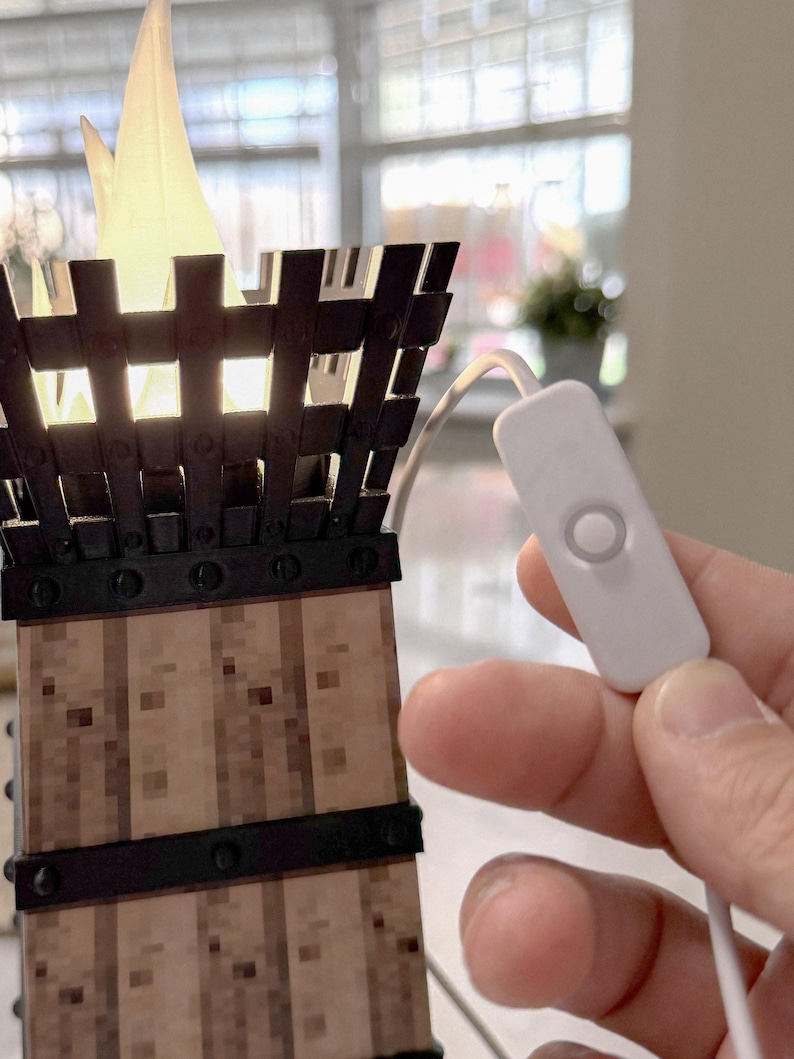 May include: A decorative lamp shaped like a torch, featuring a wooden base with metal accents and a glowing flame-shaped light. The lamp has a white cord with an on/off switch. The lamp is lit, casting a warm glow.