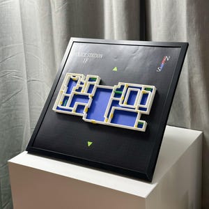 May include: A framed map of a police station's first floor, featuring a white and blue interior design. The map is set against a black background with the text "POLICE STATION 1F" and a compass rose. The frame is black.