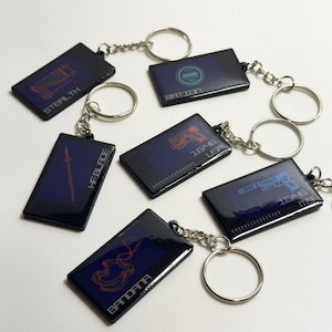 May include: Rectangular keychains with black borders and blue backgrounds. Each keychain features a different design in red or blue, with text such as "STEALTH", "HFBLADE", and "BANDANA". Silver key rings are attached.