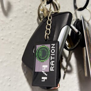 May include: A black rectangular keychain with the text "4/4 RATION" in white pixelated font, and a green pixelated circle design. The keychain is attached to a set of keys and a car key fob.