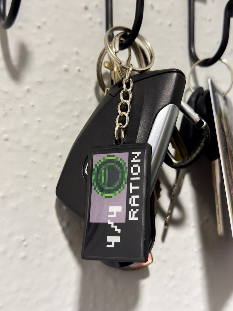 May include: A black rectangular keychain with the text "4/4 RATION" in white pixelated font, and a green pixelated circle design. The keychain is attached to a set of keys and a car key fob.