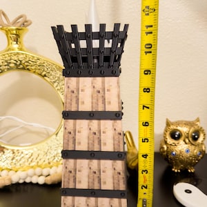 May include: A decorative candle holder with a black metal top and bands, and a light-colored, textured body. The candle holder is approximately 12 inches tall. Other decorative items are in the background.