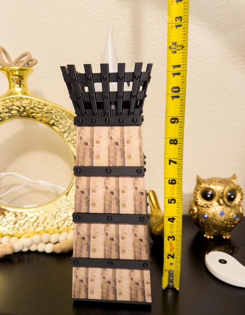 May include: A decorative candle holder with a black metal top and bands, and a light-colored, textured body. The candle holder is approximately 12 inches tall. Other decorative items are in the background.