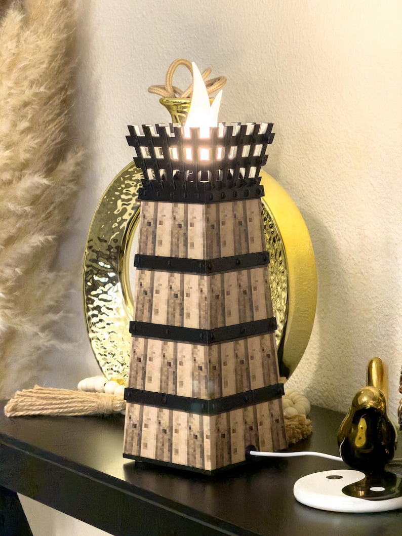 May include: A decorative lamp with a tower design. The lamp has a light brown, textured body with black bands and a black top. The top has a flame-like light. The lamp is on a black surface.
