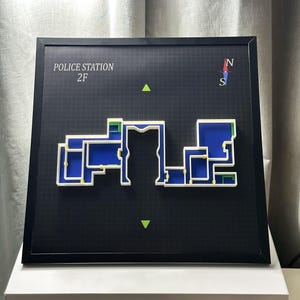 May include: A framed map of a police station's second floor, featuring a black background with a grid pattern. The map is white and blue, with a compass rose and the text "POLICE STATION 2F".