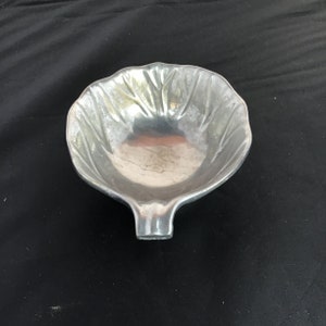 Könnte beinhalten: Eine silberne, blattförmige Schale mit einem glatten, abgerundeten Innenraum. Die Schale hat ein erhabenes, skulpturiertes Design auf der Außenseite, das an eine Blume erinnert.