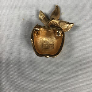 K&ouml;nnte beinhalten: Goldfarbener Apfel-Brosche mit einem Blattdesign. Die R&uuml;ckseite der Brosche hat eine Nadel und einen Verschluss.