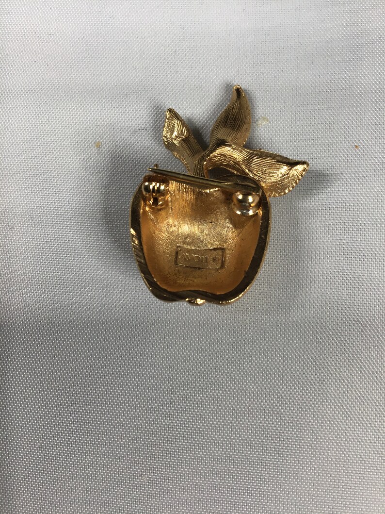 K&ouml;nnte beinhalten: Goldfarbener Apfel-Brosche mit einem Blattdesign. Die R&uuml;ckseite der Brosche hat eine Nadel und einen Verschluss.