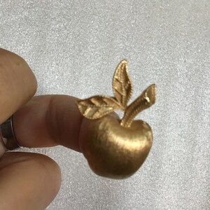 K&ouml;nnte beinhalten: Eine goldfarbene Apfelbrosche mit einem detaillierten Blattdesign. Die Brosche ist ein schlichtes und elegantes Schmuckst&uuml;ck.