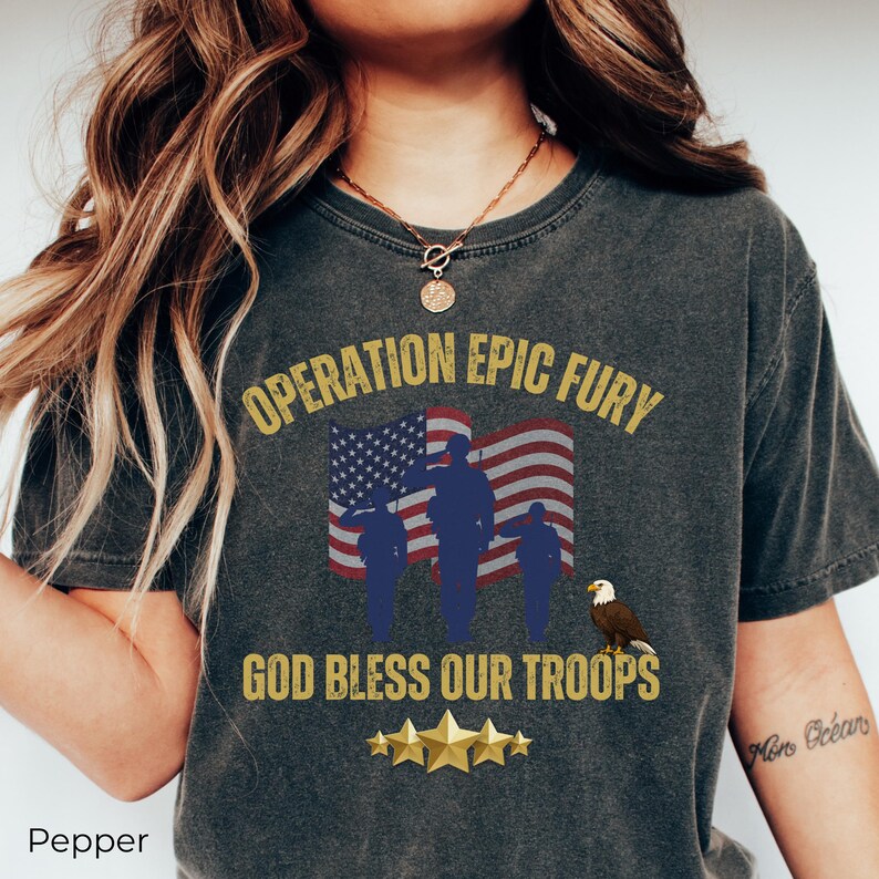 May include: Dark gray t-shirt with the text "OPERATION EPIC FURY" above an American flag and silhouettes of soldiers. Below, it reads "GOD BLESS OUR TROOPS" with gold stars and an eagle.