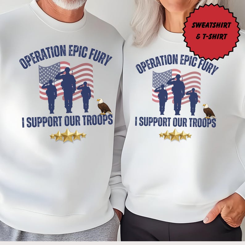May include: White sweatshirt featuring the text "OPERATION EPIC FURY" above an illustration of soldiers saluting in front of an American flag. The text "I SUPPORT OUR TROOPS" is below the illustration, with gold stars at the bottom.