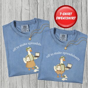 May include: Two blue crewneck t-shirts featuring a graphic of a goose wearing glasses, a green visor, and a tan outfit, holding a laptop and a clipboard. The text "off to make spreadsheets" is printed in white above the goose illustration.