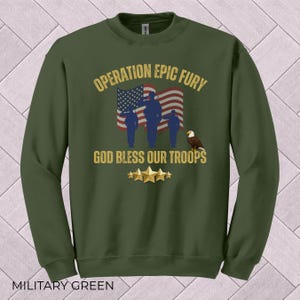 May include: Military green sweatshirt with the text "OPERATION EPIC FURY" and "GOD BLESS OUR TROOPS." The design includes an American flag, silhouettes of soldiers, an eagle, and gold stars. The sweatshirt is a crew neck.