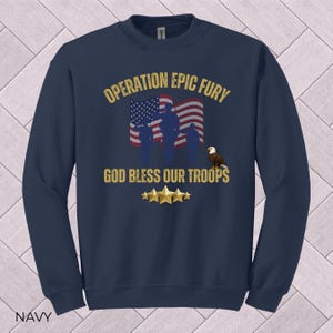 May include: Navy blue sweatshirt with the text "OPERATION EPIC FURY" and "GOD BLESS OUR TROOPS". The design includes an American flag, silhouettes of soldiers, an eagle, and gold stars. The word "NAVY" is at the bottom.