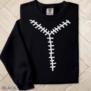 Könnte beinhalten: Schwarzes Sweatshirt mit einem weißen, genähten Reißverschluss-Design. Das Sweatshirt ist gefaltet und hat ein Etikett in der oberen rechten Ecke. Das Wort "BLACK" ist unten links aufgedruckt.
