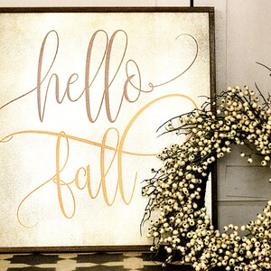 May include: A wooden sign with a rustic background and the words "hello fall" written in a cursive font. The sign is decorated with a white berry wreath.