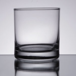 May include: A clear glass tumbler with a thick base. The glass is empty and has a slight reflection of the background.